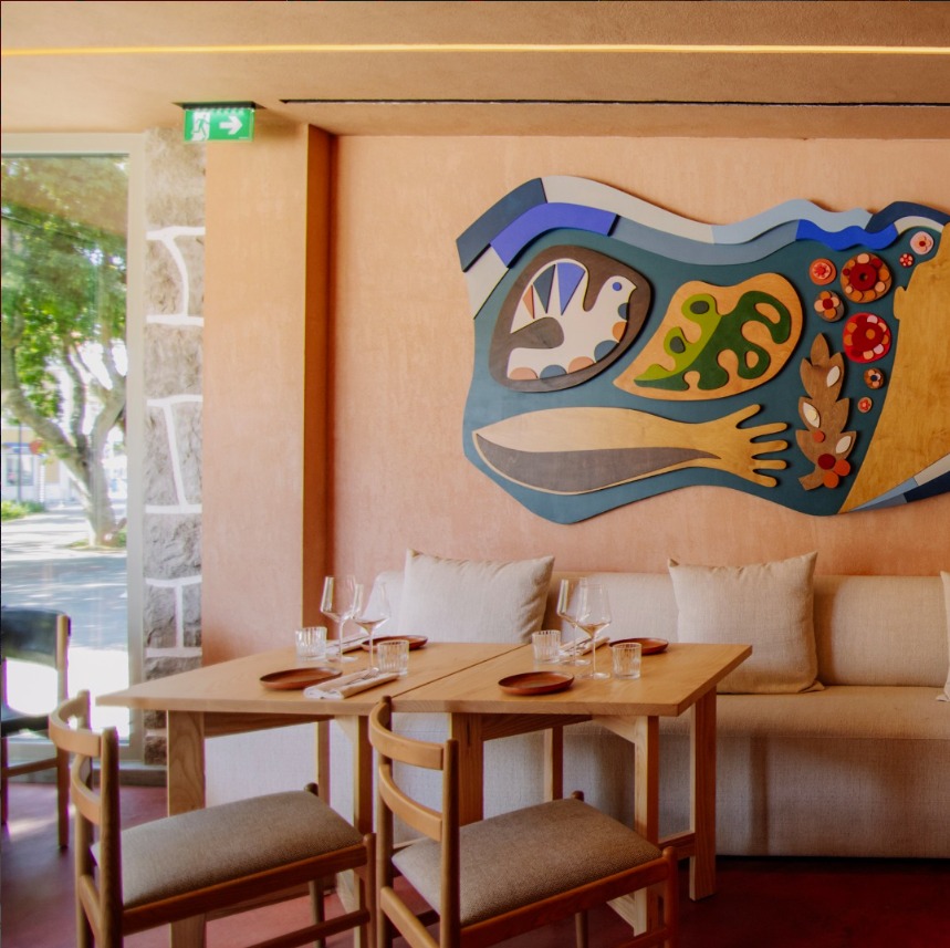 Sala luminosa do Madrasta, em Paço de Arcos, com mesas de madeira e parede decorada